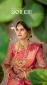Bride wearing a pink saree with heavy gold jewelry, hennaed hands, framed by green leaves.