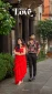 Couple posing outdoors: woman in a red ruffled dress and sandals, man in a dark floral shirt and trousers beside a columned facade, with Chromatic Love logo above.