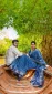 Couple sitting in a wooden boat under lush green trees; woman in a blue patterned saree, man in a striped shirt, posing by the water.
