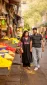 Couple walking hand in hand past vibrant flower stalls on a busy street market.