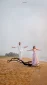 Man and woman stand on a fallen log at the beach with arms outstretched, sea behind them.