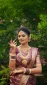 Bride in a maroon saree with heavy gold jewelry, showing hennaed hands in a graceful pose outdoors