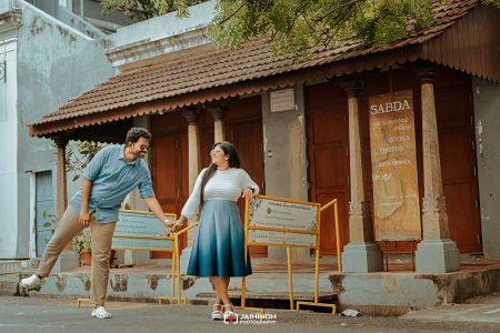 Young couple holding hands and smiling in front of a storefront with a SABDA sign and orange barriers nearby.