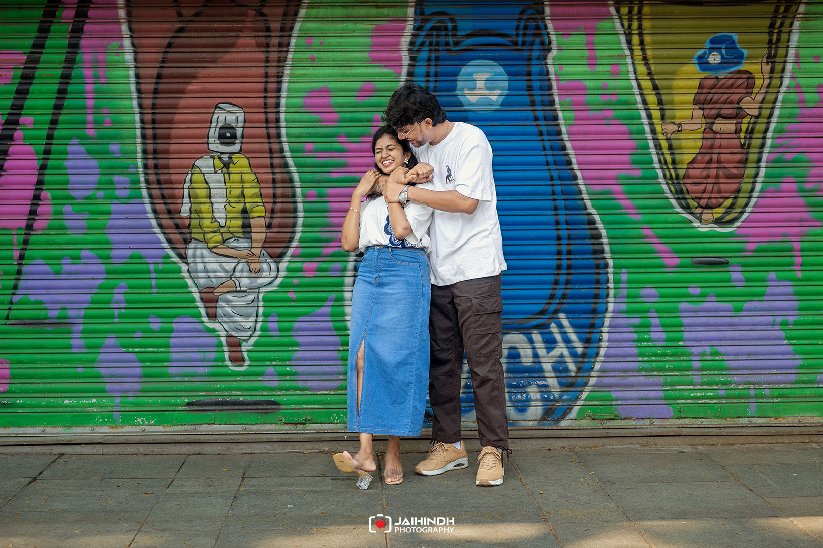 Couple embracing and laughing in front of a bright graffiti mural on a metal shutter.