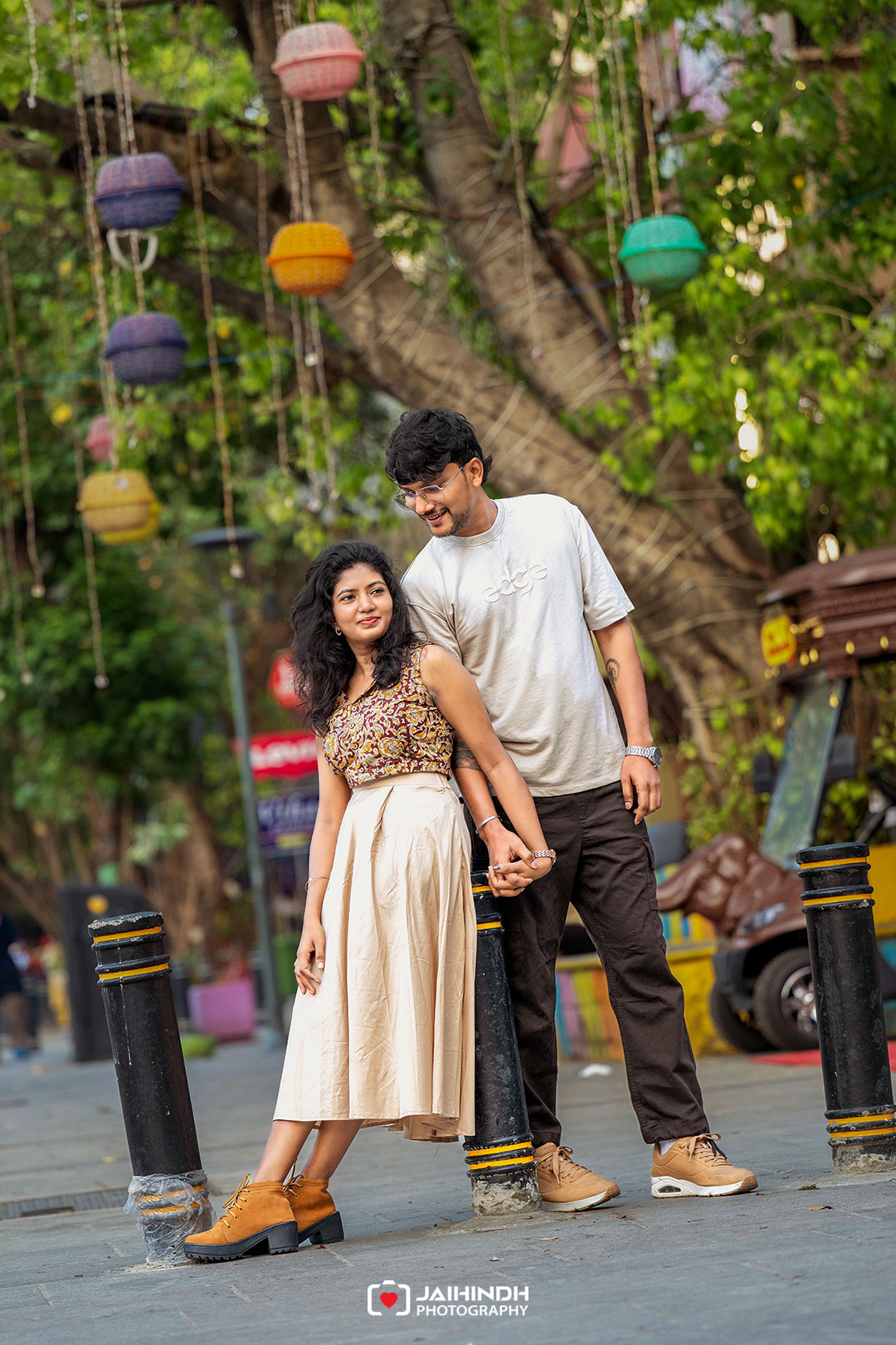 Couple walking hand in hand on a city street with colorful hanging lanterns above them.