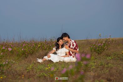Couple sitting in a wildflower field, leaning against each other and smiling.