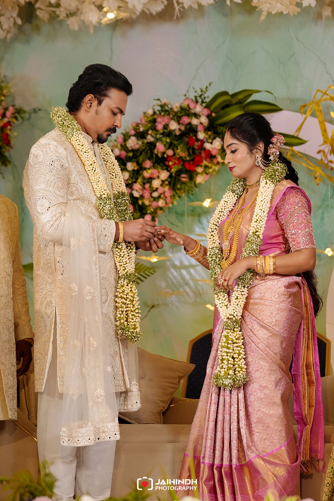 Bride and groom exchanging rings during a traditional indian wedding, both wearing ornate attire and flower garlands.