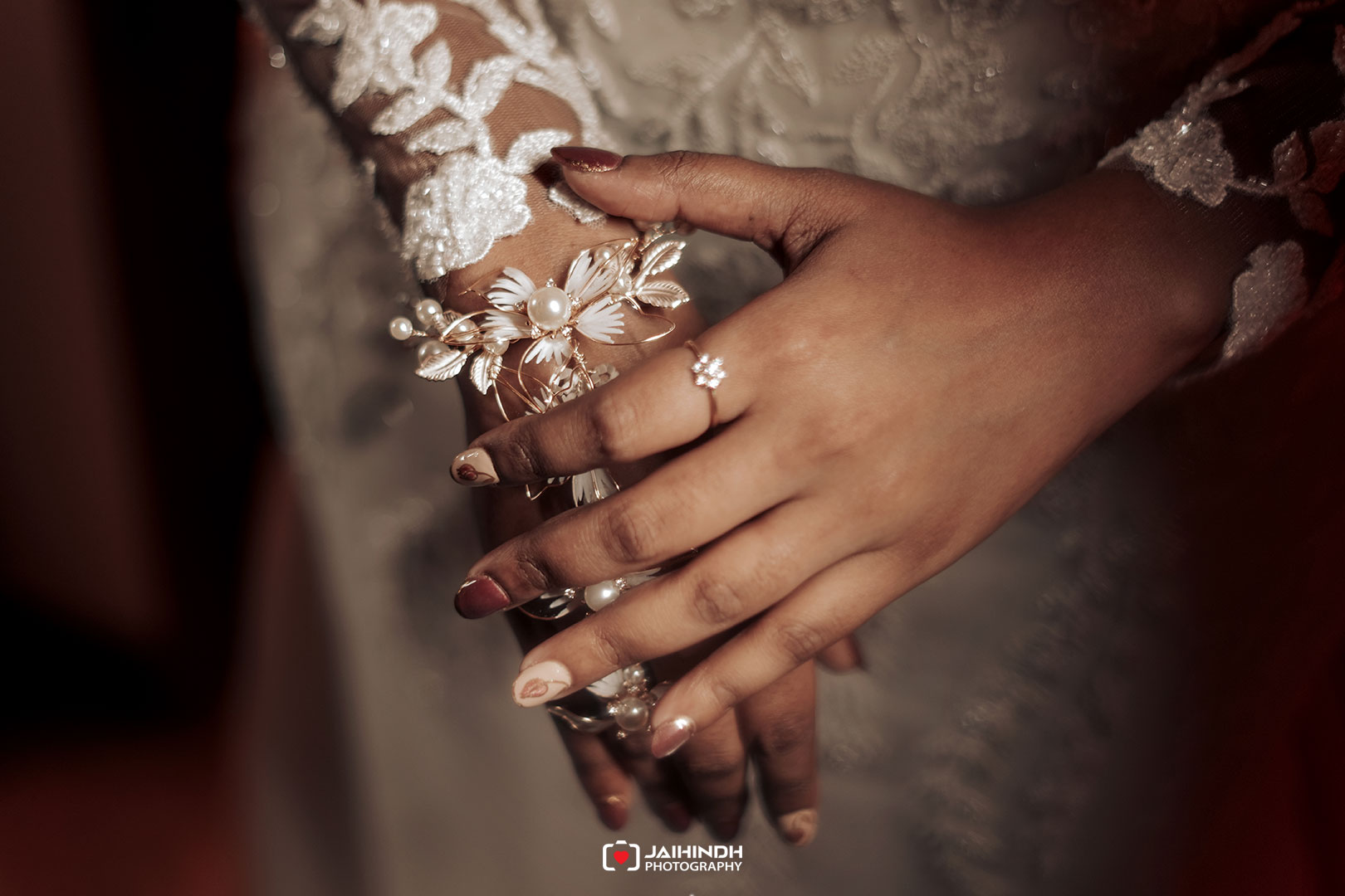 Close-up of hands wearing a floral pearl bracelet and ring, rest of lace dress in the background, wedding jewelry visible