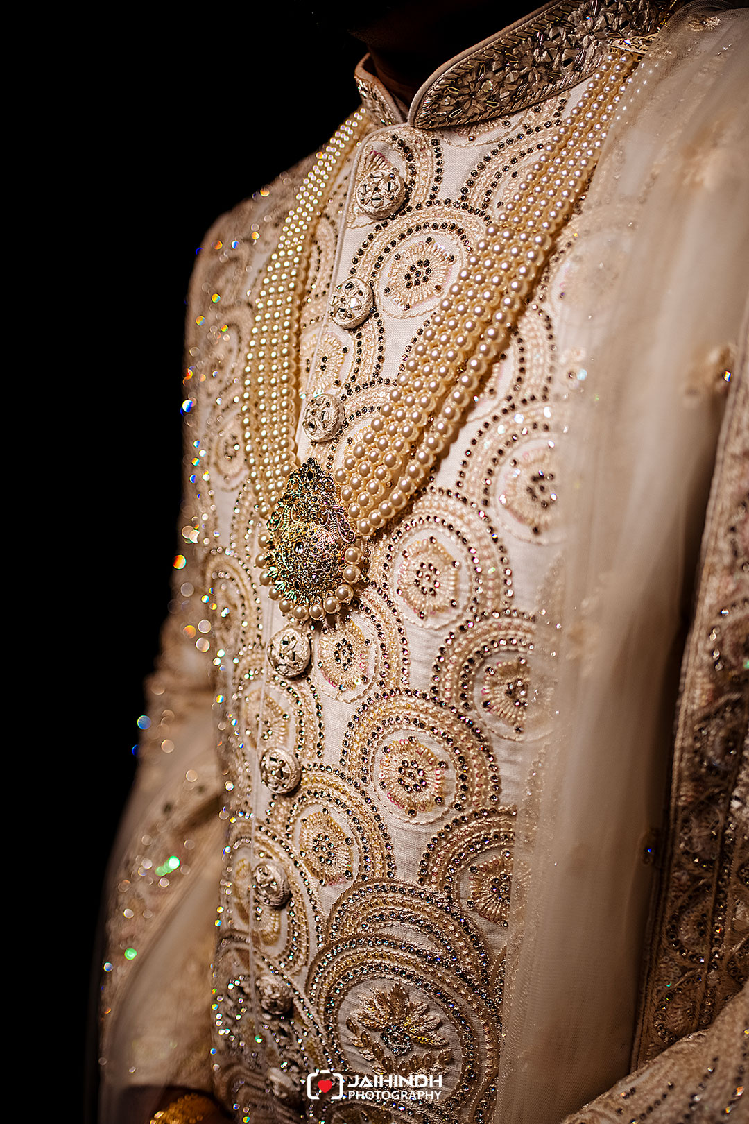 Close-up of a cream-colored, beaded wedding outfit with layered pearl necklaces and a jeweled brooch centerpiece.