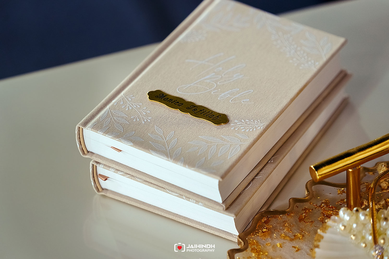 Beige embossed wedding album stack with a gold nameplate on the top book and white floral patterns.