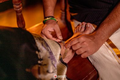 Close-up of hands fastening a gold anklet on a person’s ankle during a traditional ceremony.