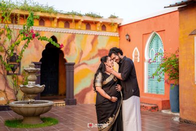 Couple embracing in a colorful courtyard; the pregnant woman leans into her partner as he touches her face.