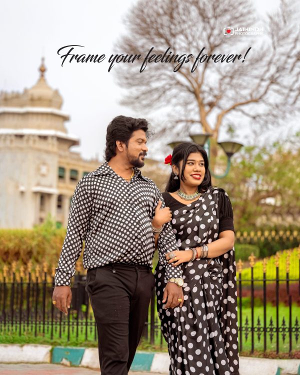 Couple in black-and-white polka dot outfits posing outdoors in a park, with a historic building and bare trees in the background.