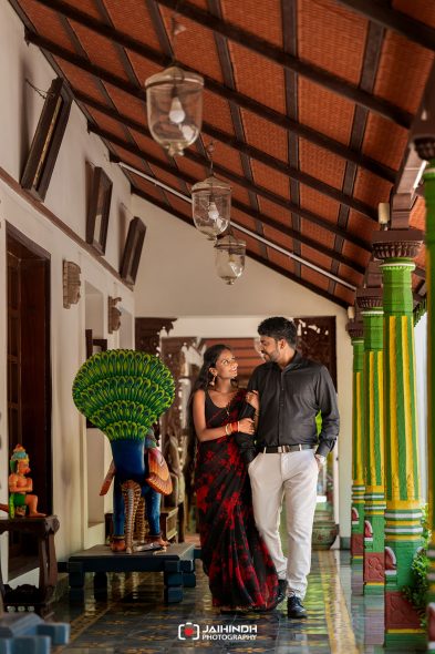 A couple walks arm-in-arm through a colorful temple-like corridor with green and yellow pillars and hanging lanterns.