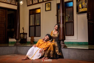 Couple in traditional Indian dress sit on a porch step, the woman leaning on the man's shoulder as they relax together.