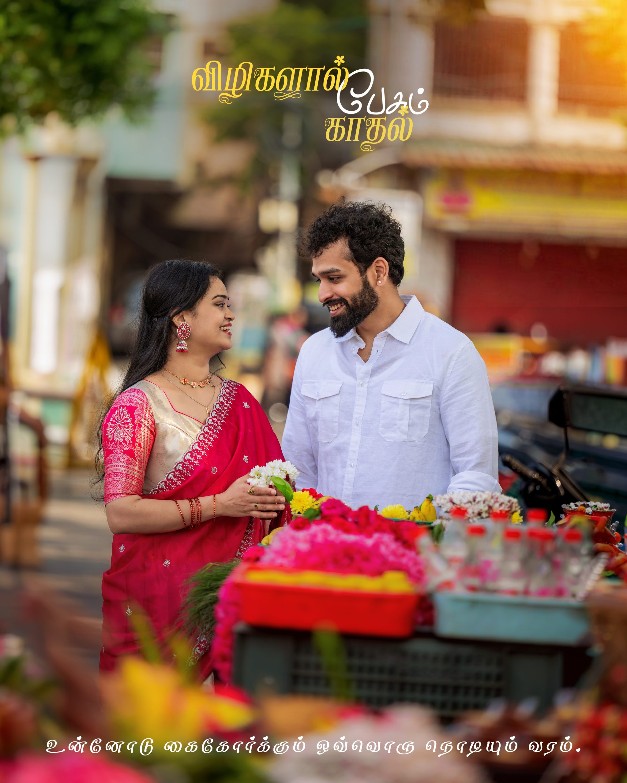 Couple in traditional attire smiles at a flower stall on a busy street, with decorative Tamil text across the top and bottom of the image.