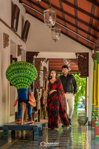 Couple walking down a colorful corridor in traditional attire, smiling and holding hands.