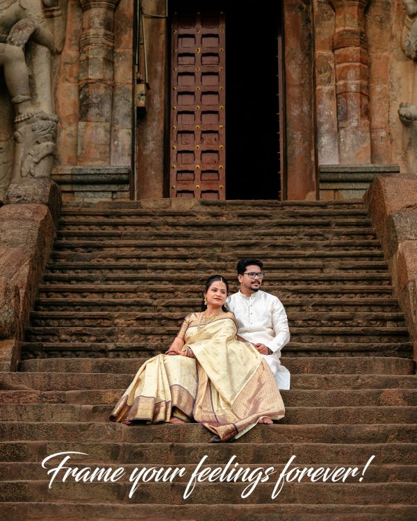 Couple in traditional Indian attire sitting on weathered temple stairs in front of an ornate doorway with carved pillars; wedding scene.