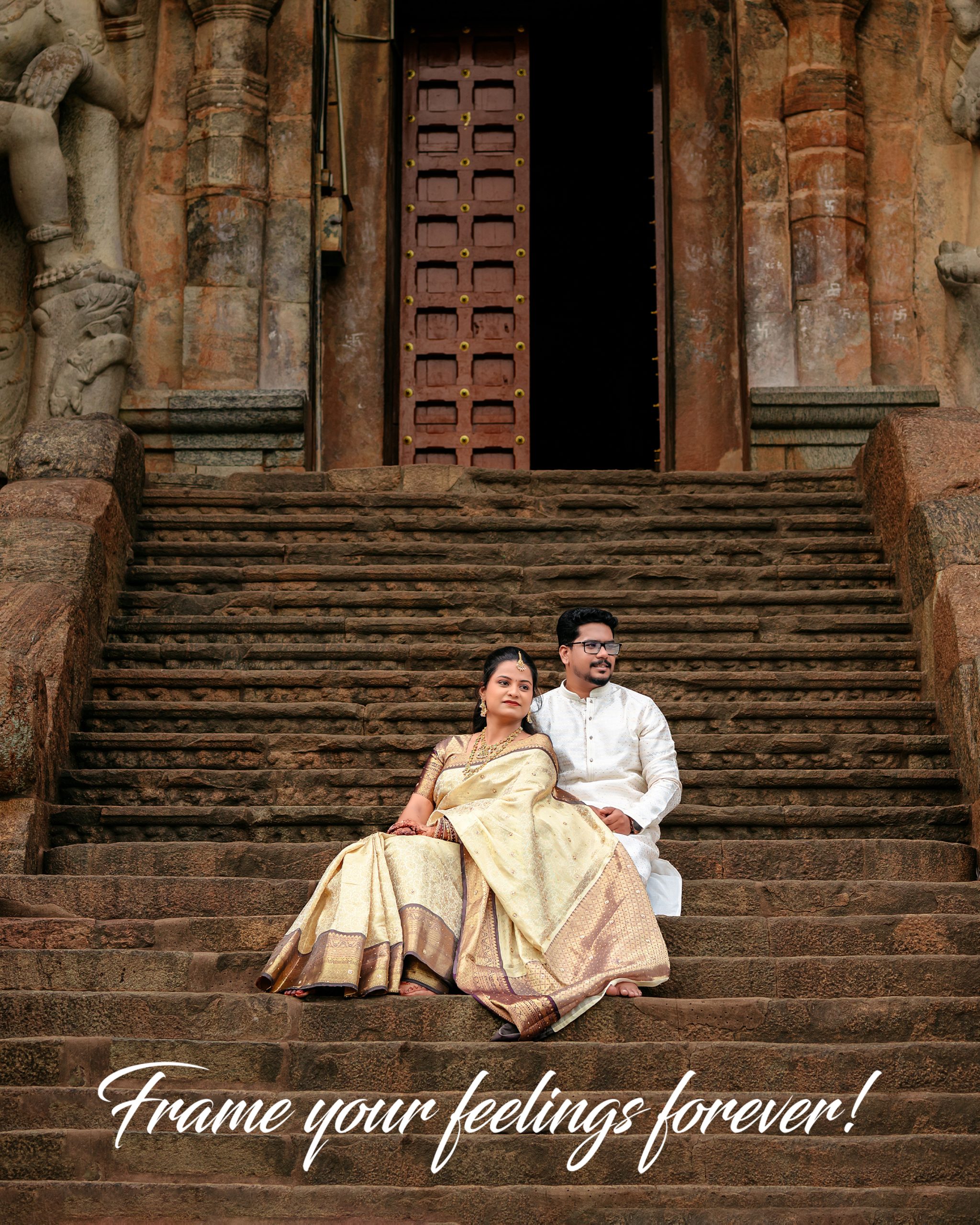 Couple in traditional Indian attire sitting on weathered temple stairs in front of an ornate doorway with carved pillars; wedding scene.