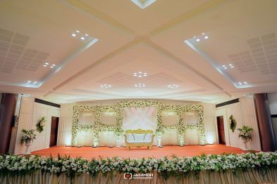 Wedding stage with floral arch frames, white drapery, and a white-and-gold sofa on a red carpet.