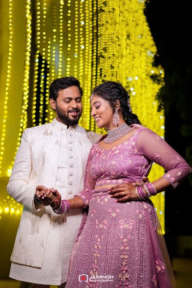 Couple in traditional Indian attire dancing together at night with warm yellow string lights in the background, smiling and holding hands.
