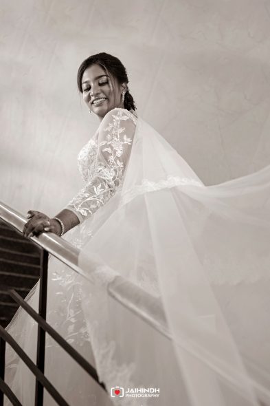 Bride in a lace wedding gown and flowing veil descending a staircase, smiling.