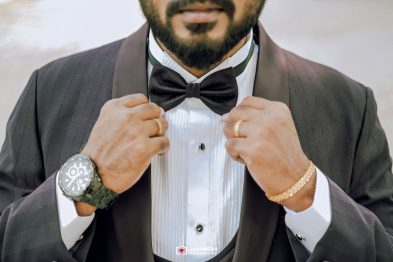 Man in a tuxedo adjusts a black bow tie, focusing on the knot.