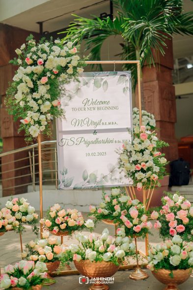 Wedding welcome board framed by lush white and pink flowers, with greenery and a date that reads 'Welcome to our new beginning' and '10.02.2025'.