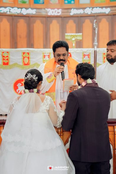 Priest in bright robes officiates a church wedding as the bride and groom hold hands at the altar.