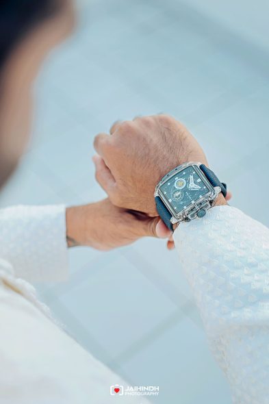Close-up of a man’s wrist wearing a square blue-faced watch with a blue strap. I