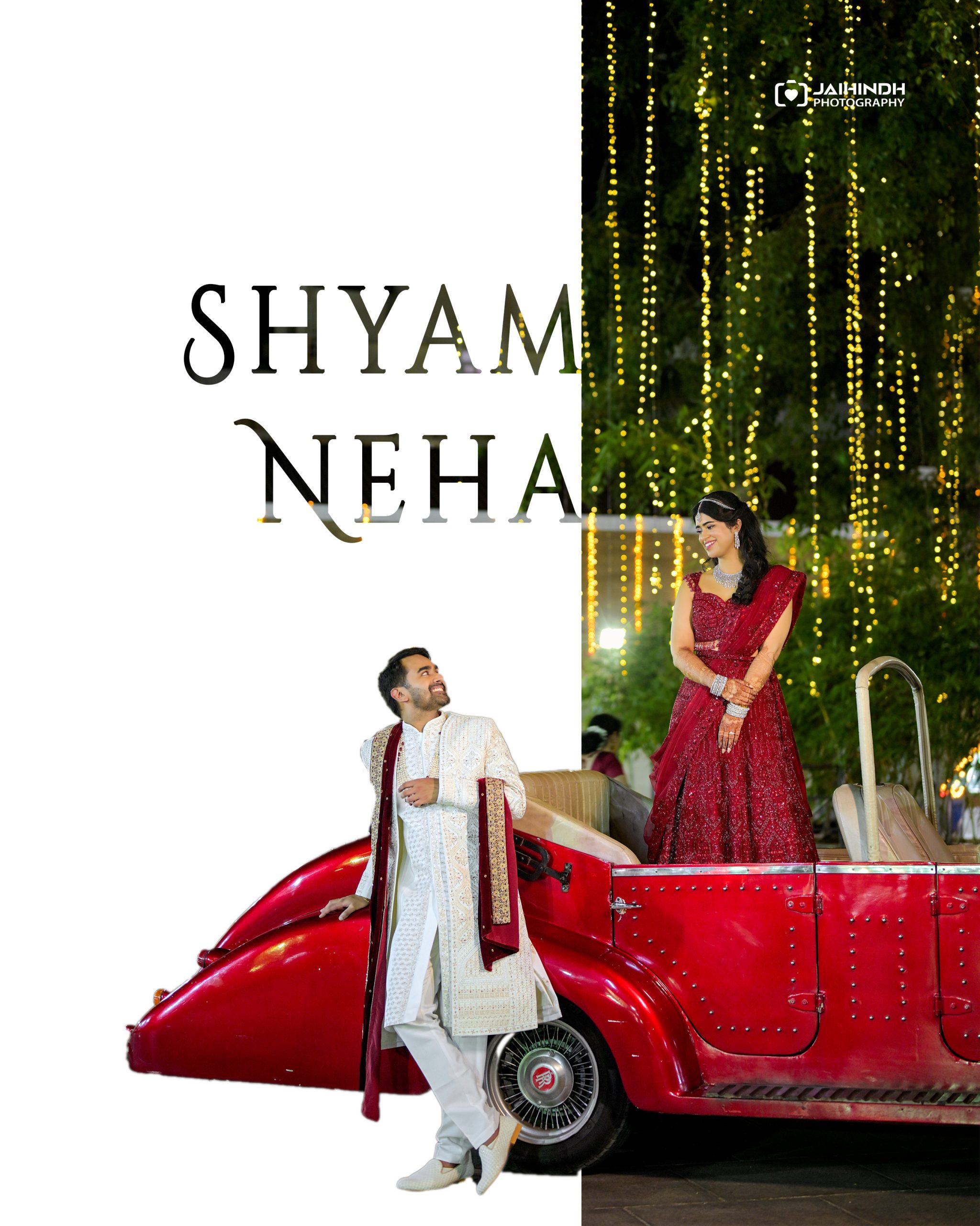 Bride and groom in traditional Indian attire pose beside a bright red vintage car under string lights at a wedding.